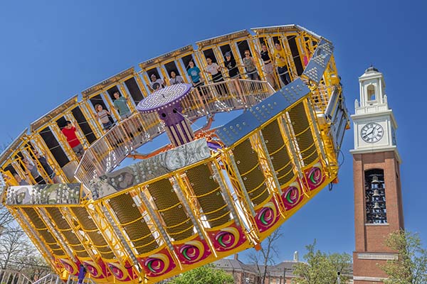 students ride in a Tilt-a-Whirl in front of Pulley Tower during SpringFest
