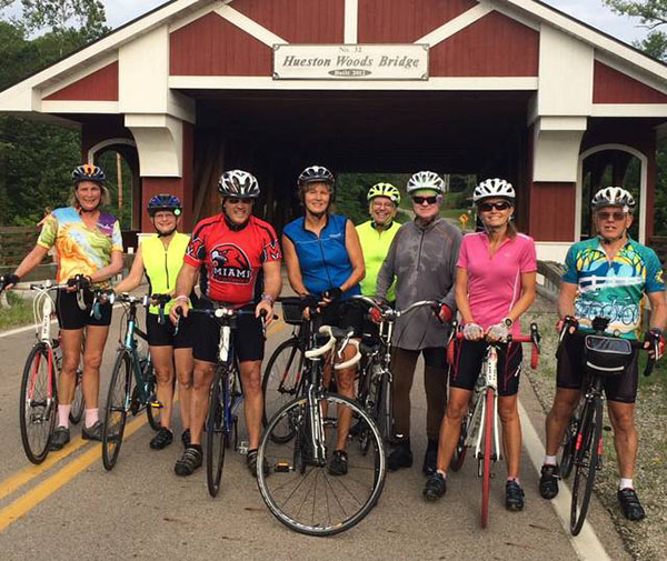 Helaine Alessio, Renate Crawford, Greg Crawford, and several other people pose on their bikes in front of Houston Woods Covered bridge