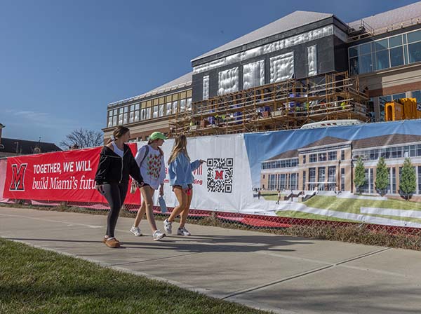 Together We Will build banner on red construction fence in front of McVey Data Science building and 3 students walking in front